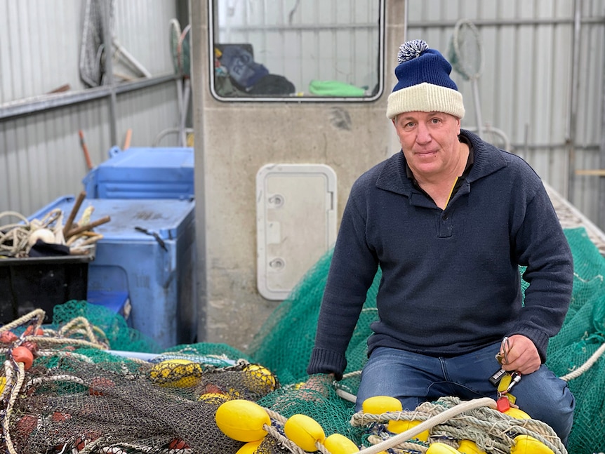 Picture of Bruce kneeling on top of colourful fishing nets in his boat.