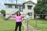 Deb frecklington stands out the front of a house with her hands in the air. 