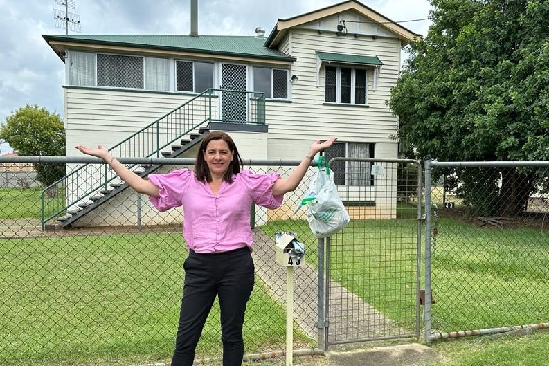 Deb frecklington stands out the front of a house with her hands in the air. 