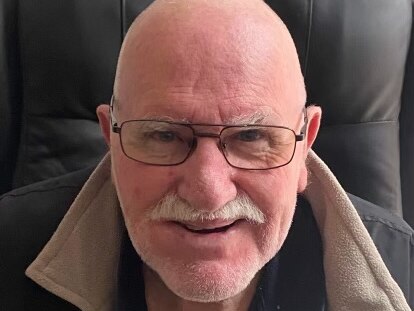 A bald headed Caucasian man wearing glasses with a grey moustache