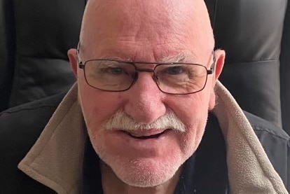 A bald headed Caucasian man wearing glasses with a grey moustache