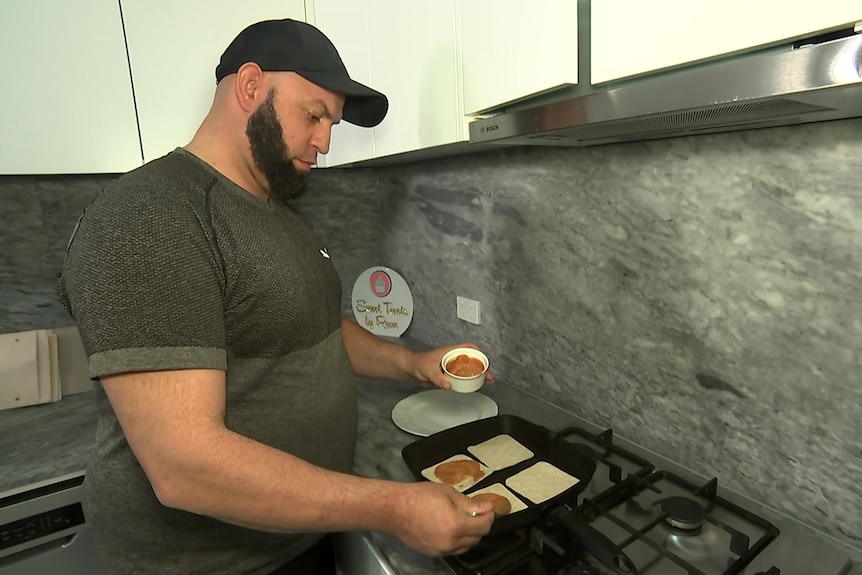 a man wearing a cap standing over a stove cooking