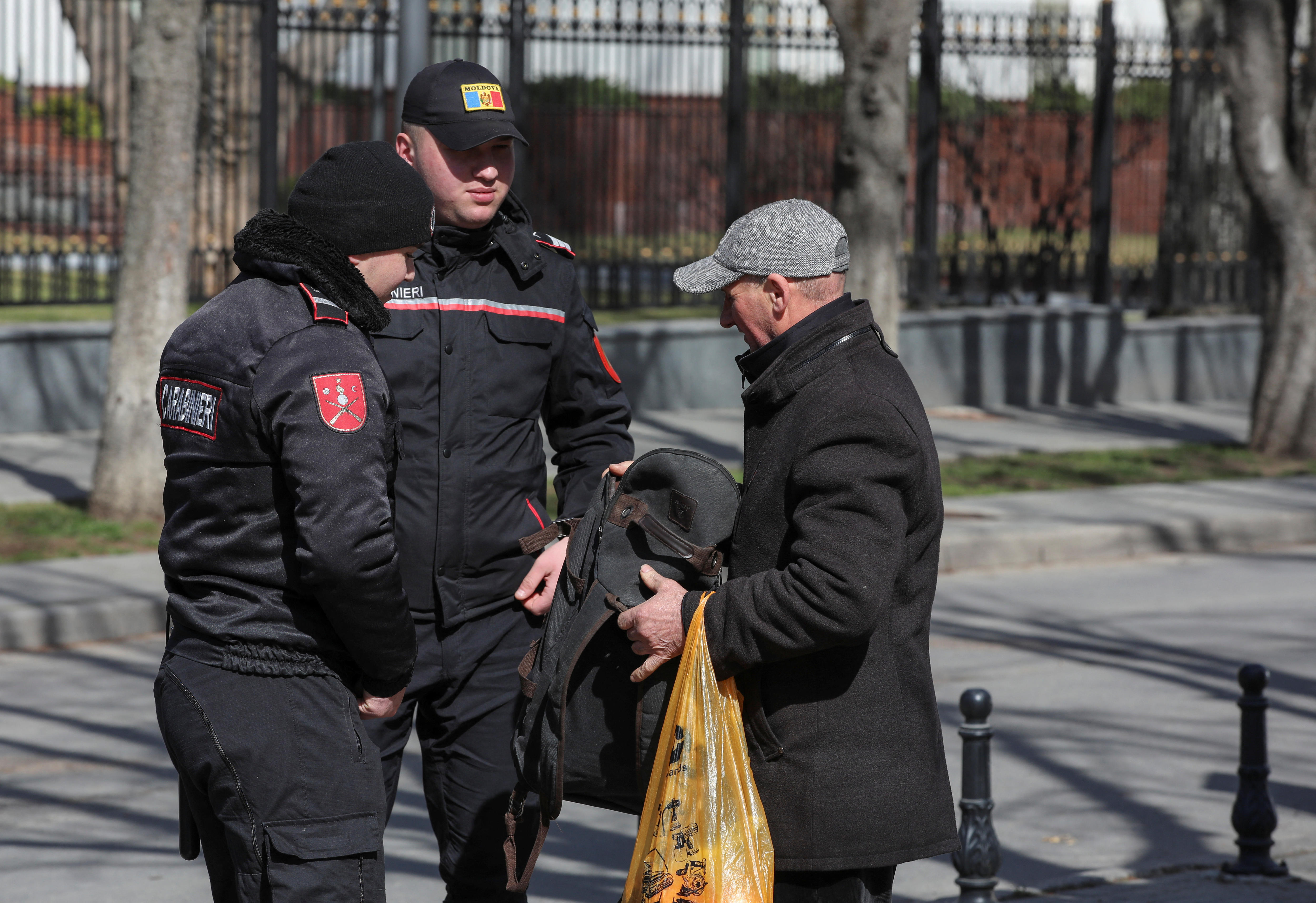 Two police officers check the bags of a man.