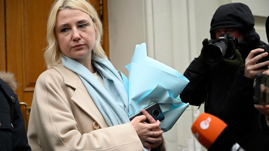 Woman in beige coat holds pile of bue papers 