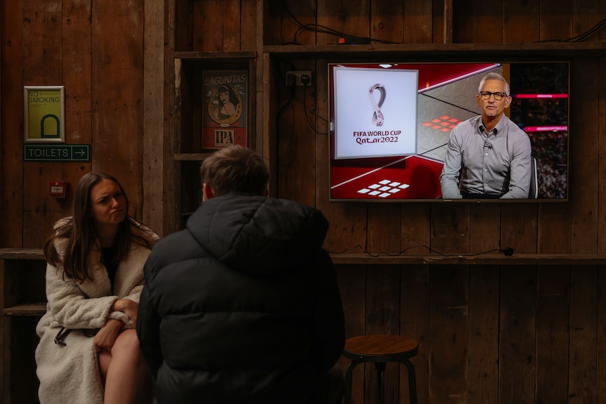 Gary Lineker on a screen at a pub. Two patrons aren't watching.