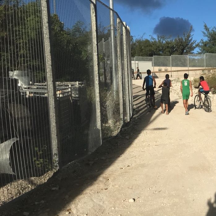 Children walk and ride bikes past a fence