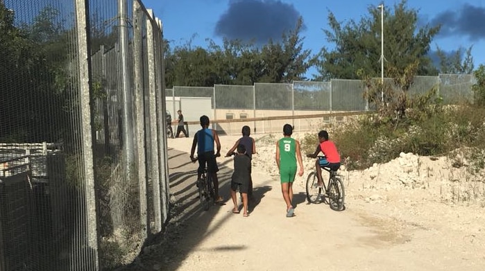 Children walk and ride bikes past a fence