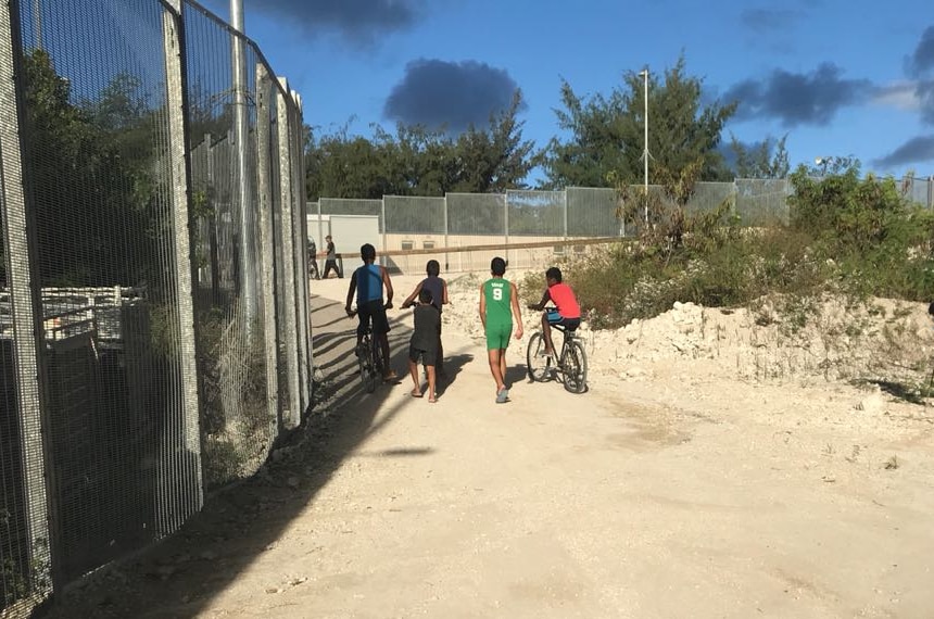 Children walk and ride bikes past a fence