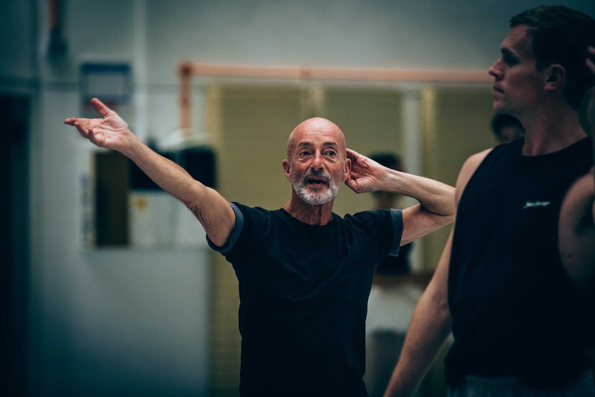 Choreographer Graeme Murphy with one arm extended and the other at his ear at a ballet rehearsal.