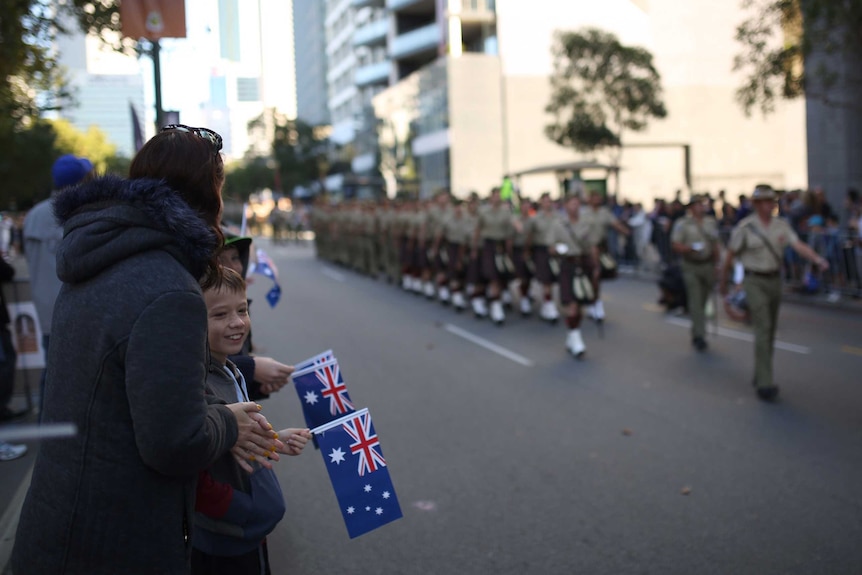 A boy and a woman holding mini-Australian flags watch an Anzac Day march.