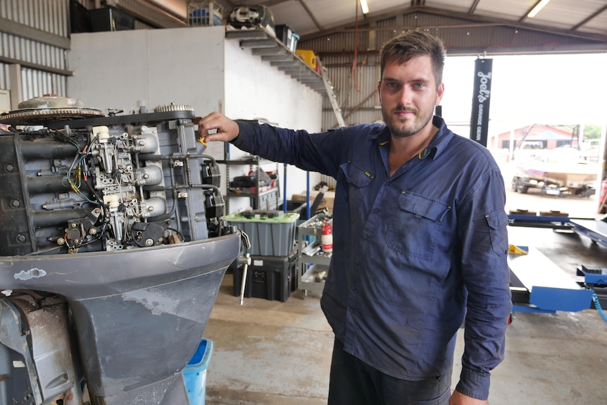 A man next to an outboard motor with its cover off