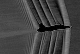 Grainy silhouette image of a jet with visible soundwaves peeling back from the front of the jet.