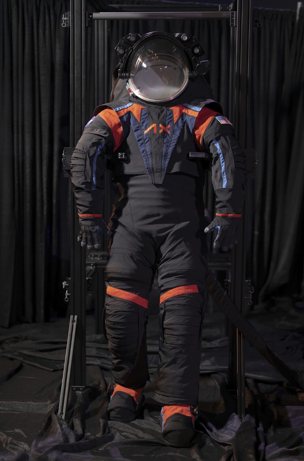 a dark grey space suit has pops of orange and blue on the shoulders and chest.