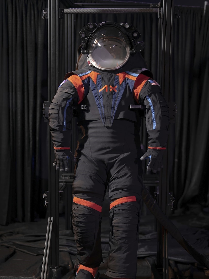 a dark grey space suit has pops of orange and blue on the shoulders and chest.