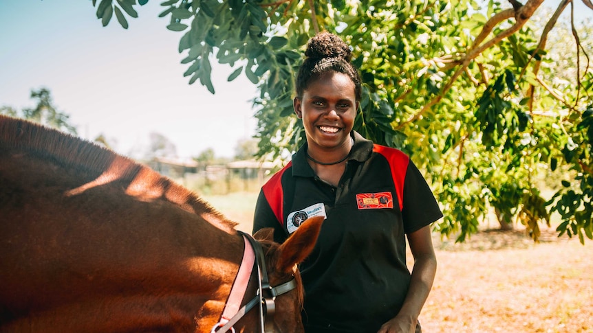 Doomadgee State School student Thomasina Foot smiling at the camera, holding a horses bridle.