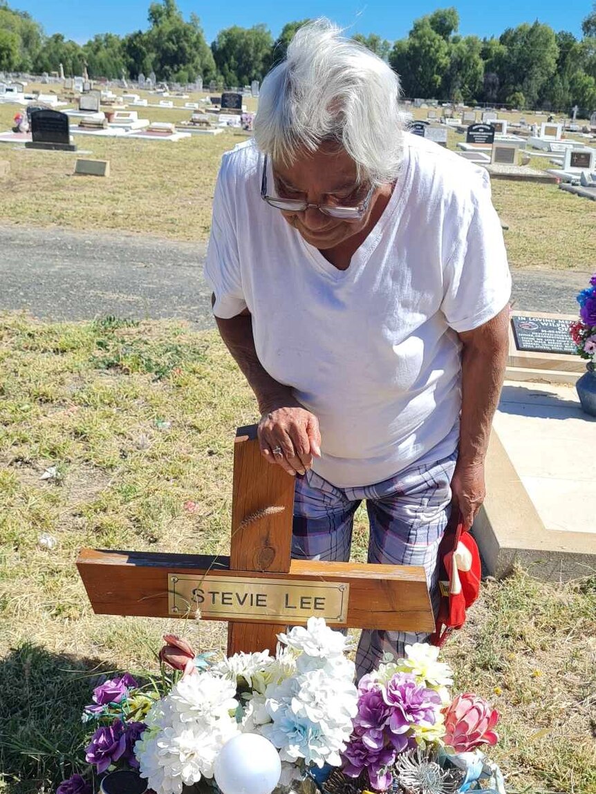 An older woman lays flowers on a grave.