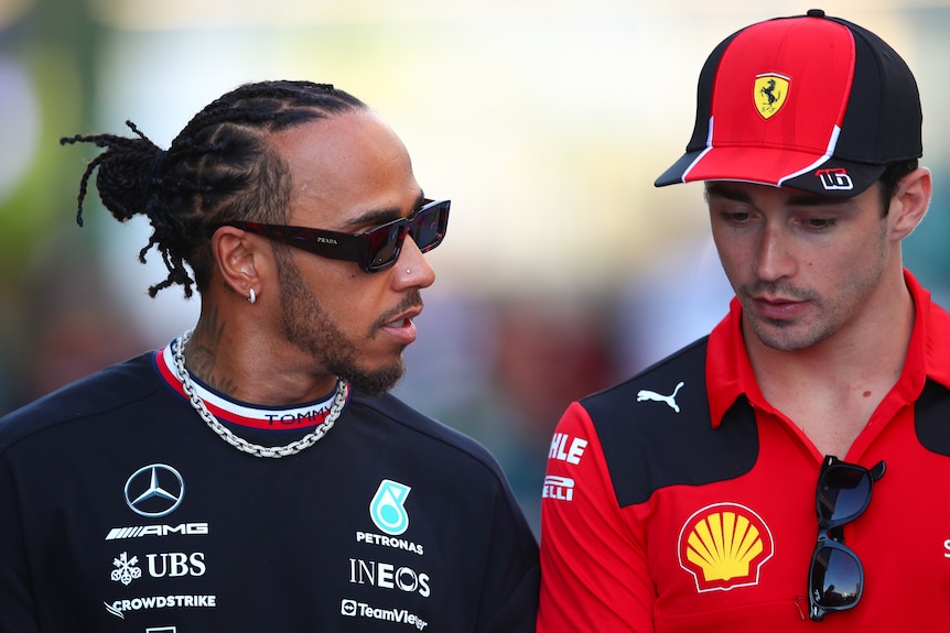 Two racing drivers, the one on the left wearing a black shirt, the other wearing red, talking to each other