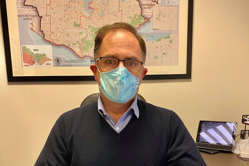 A man sitting at a desk wearing a home made face mask