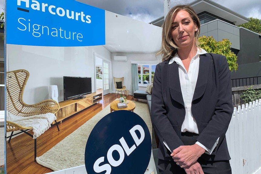 A woman stands in front of of a sold sign