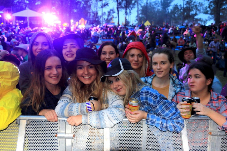 A group of girls gather near security barriers in front of a music stage.