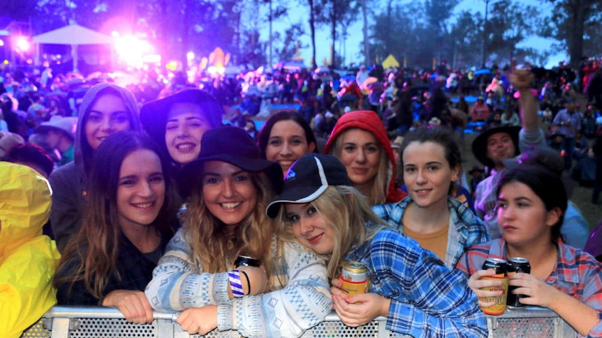 A group of girls gather near security barriers in front of a music stage.