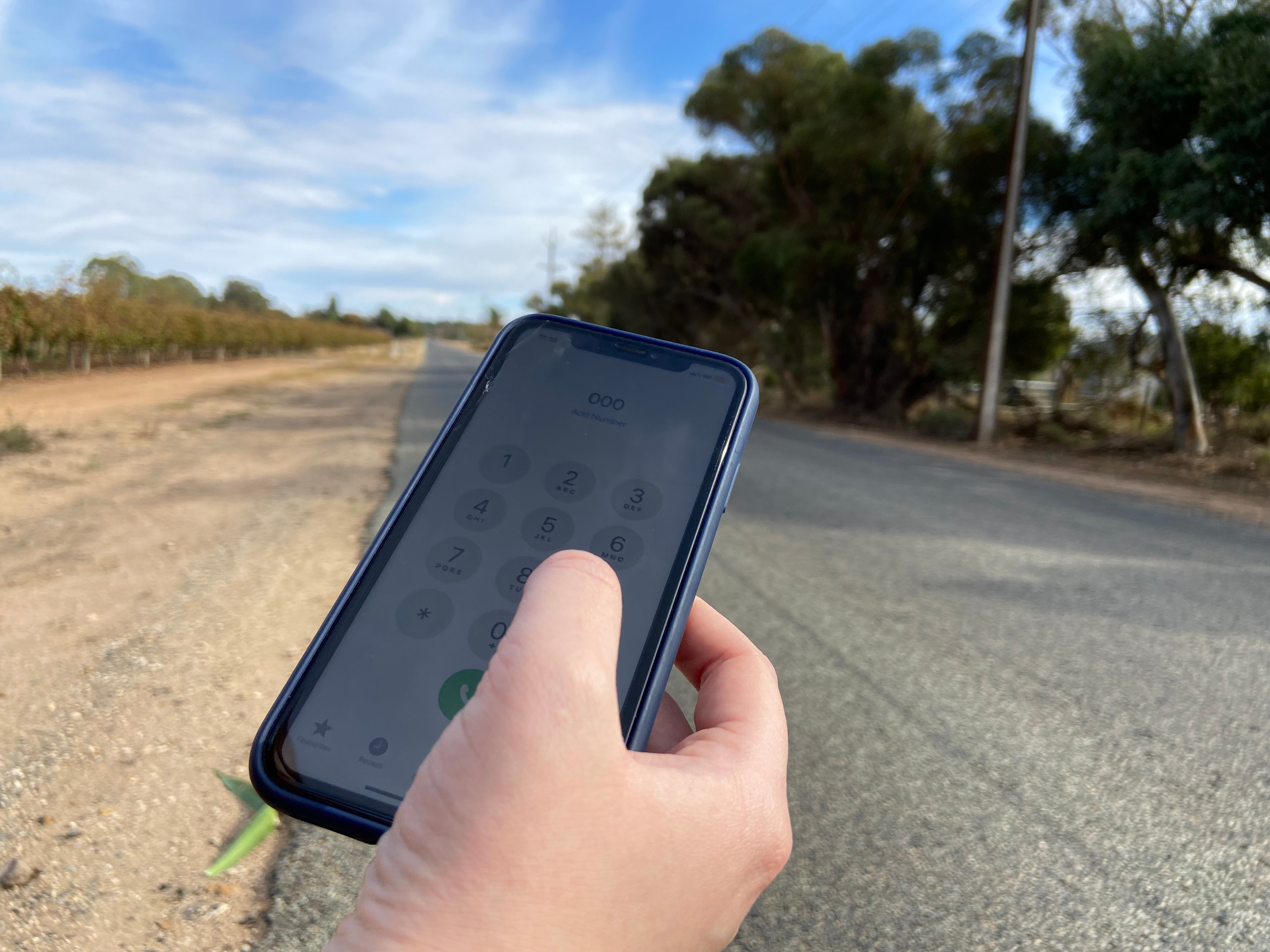 Telemóvel com 000 exibido, numa estrada secundária com vinhas ao lado.