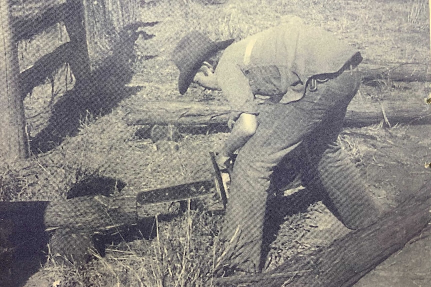 Black and white image of a young man wearing a black hat using a chainsaw.