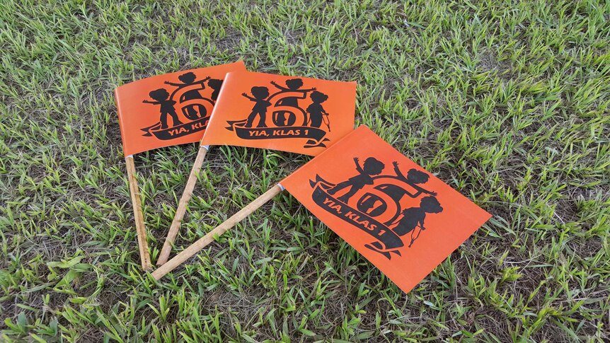 Three campaign merchandise flags lying on grass with the "6 Yia Klas 1" and logo written on them
