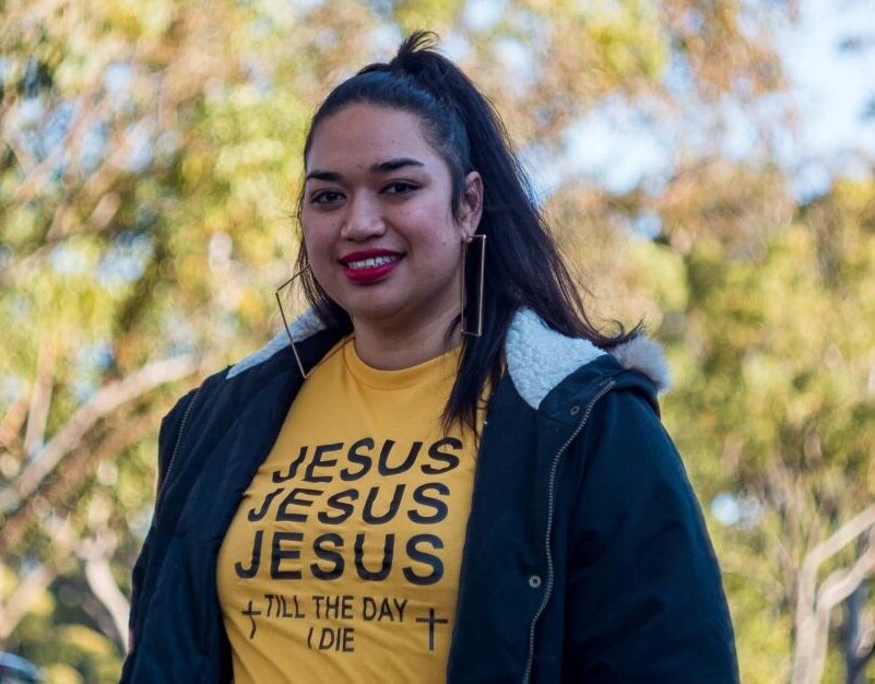Ana Makahununiu, a Tongan woman, smiling. She is wearing a t-shirt that says 'Jesus Jesus Jesus till the day I die.'
