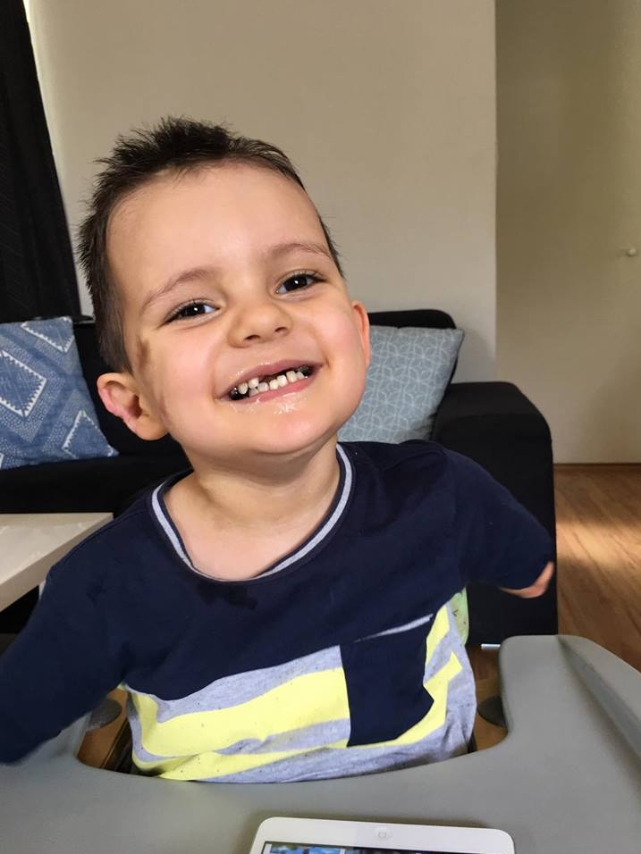 Robbie Buchan smiles in a high-chair, aged 3. He has both arms amputated.