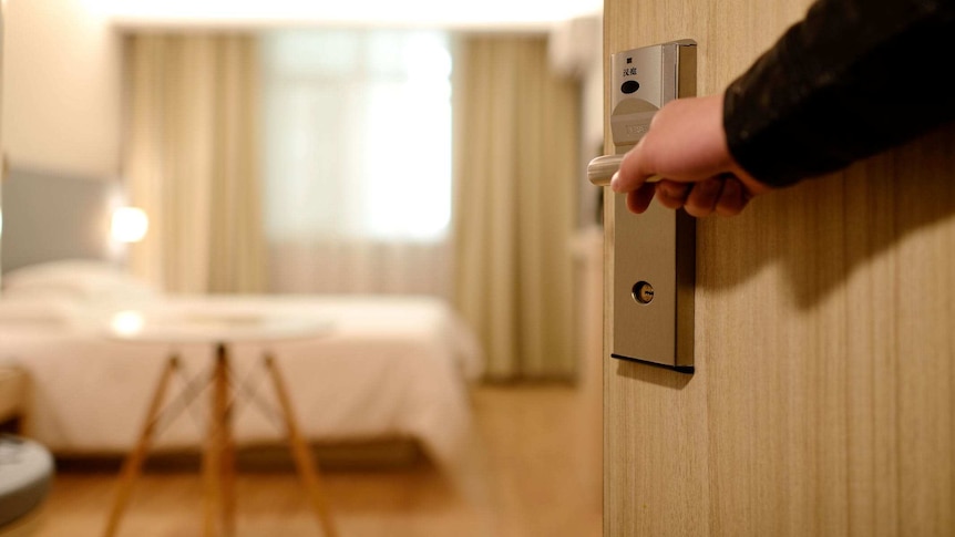 A person opens a door to reveal the interior of a hotel room.