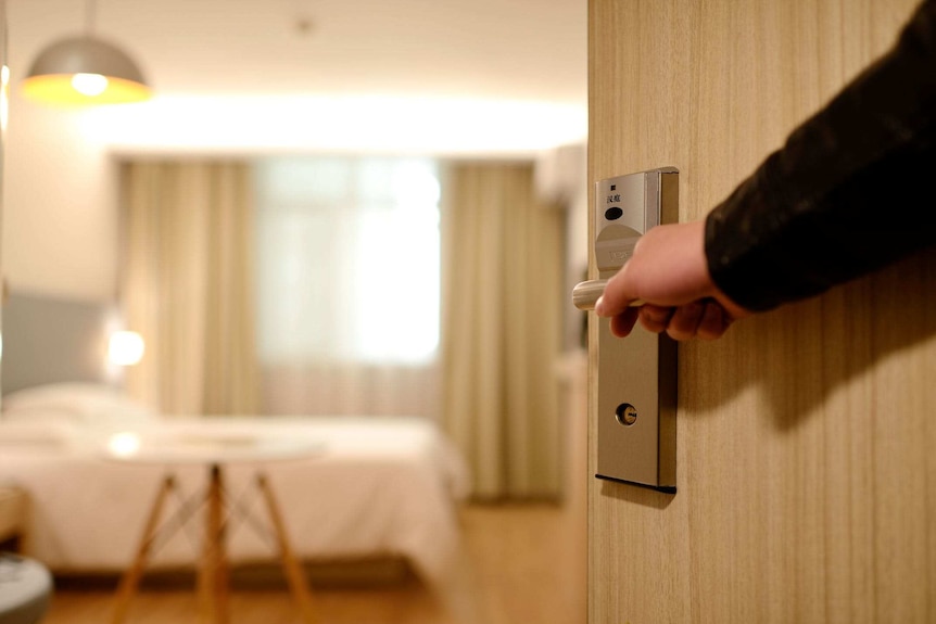 A person opens a door to reveal the interior of a hotel room.