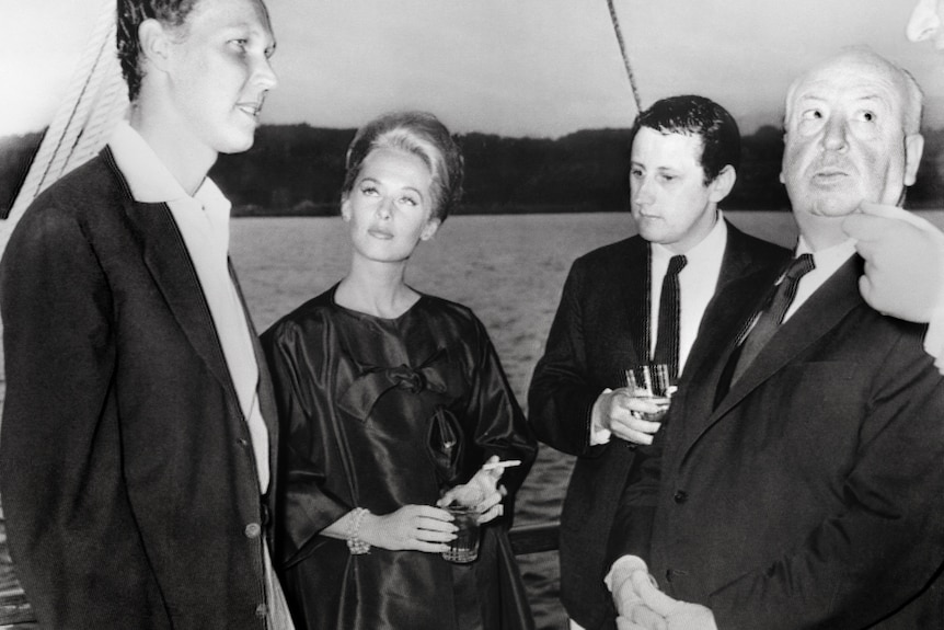 A black and white photograph of Vittorio Emanuele (left) standing with Tippi Hedren, Alfred Hitchcock and another man on a boat.