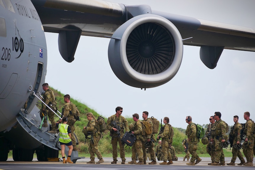 Defence Force personnel in uniform queue to board a plane