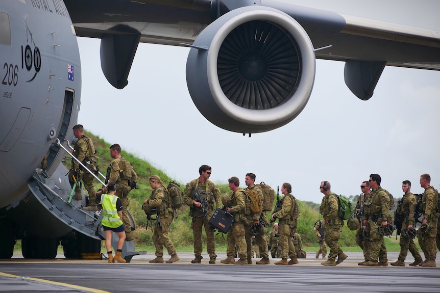 Several soldiers in uniform are seen in line, ready to board a plane