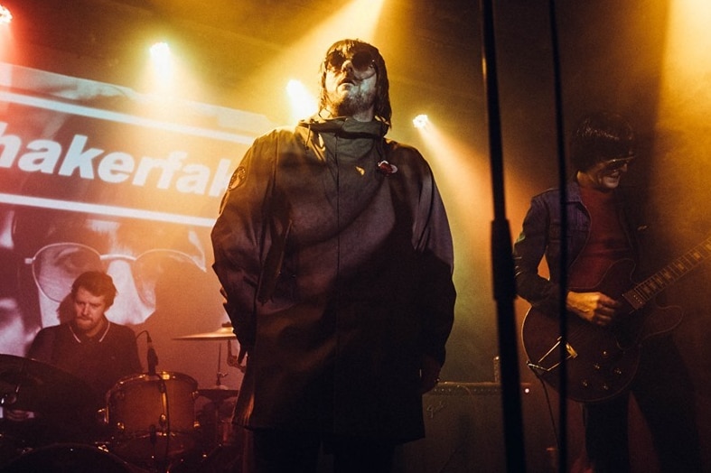 The singer of Shakerfaker looks into the distance on stage surrounded by band members under moody lighting
