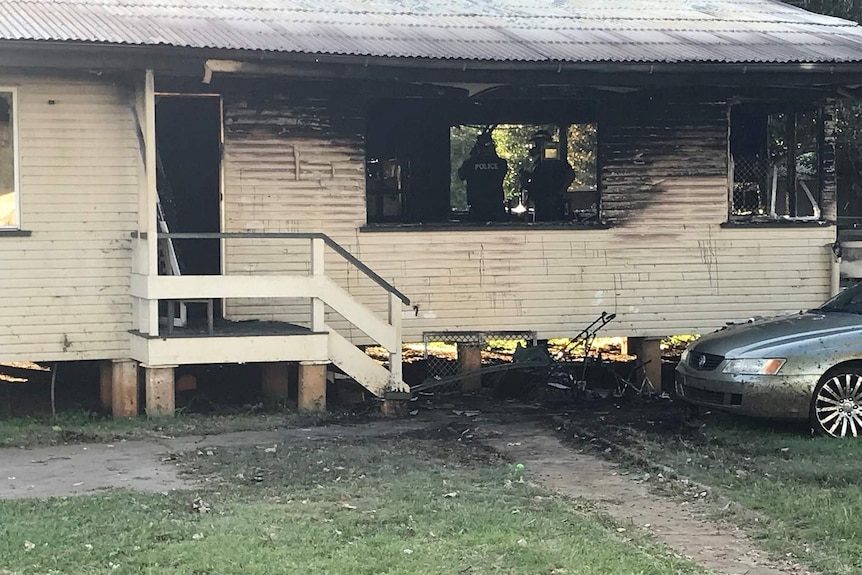 Police inspect the burnt out shell of the rear of a low set timber house.