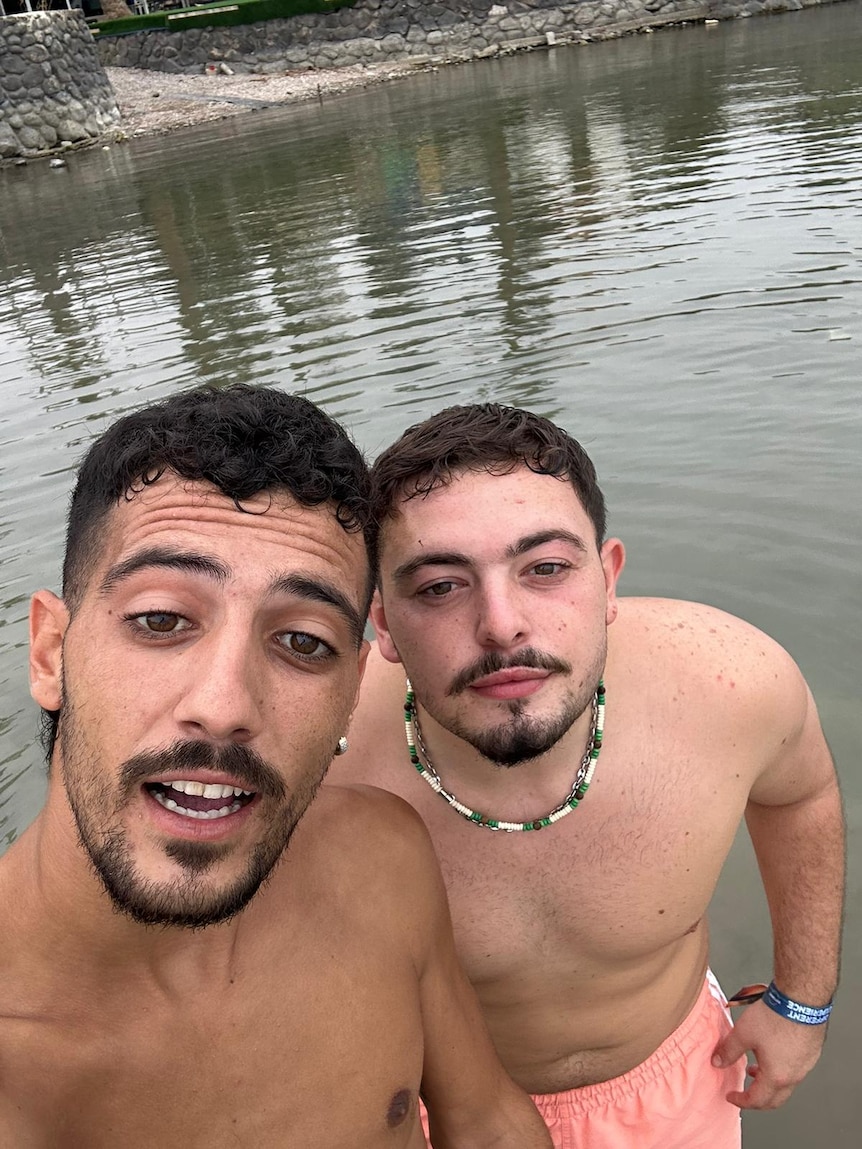 Two men stand shirtless in a river.