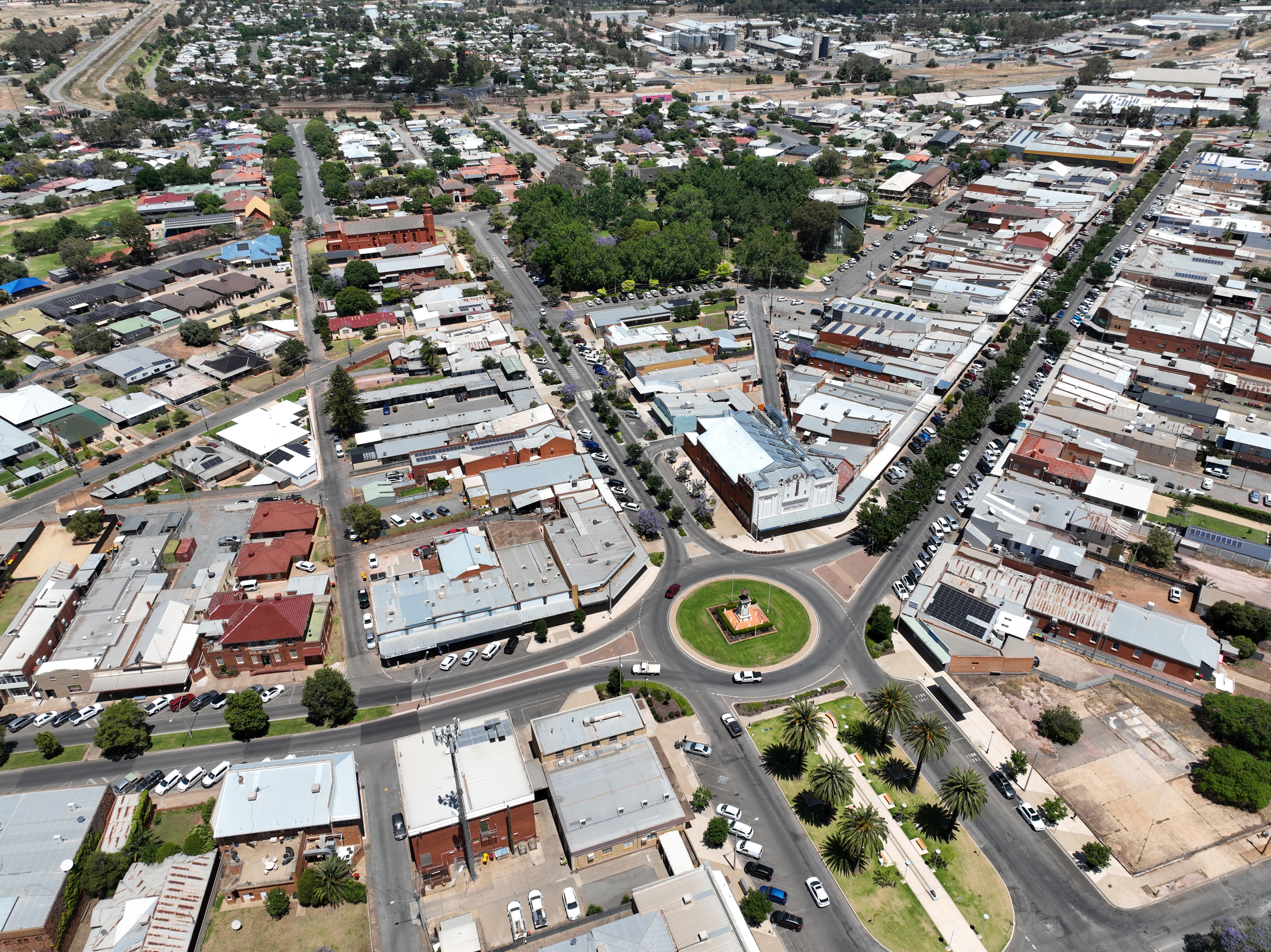Picture shows an aerial view looking down onto a rural town, roads, and roof tops are visible, as well as green open space.