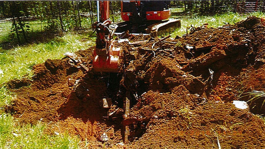 An excavator upturning a pile of waste materials and dirt.