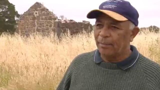 Indigenous man stands in front of stone ruin
