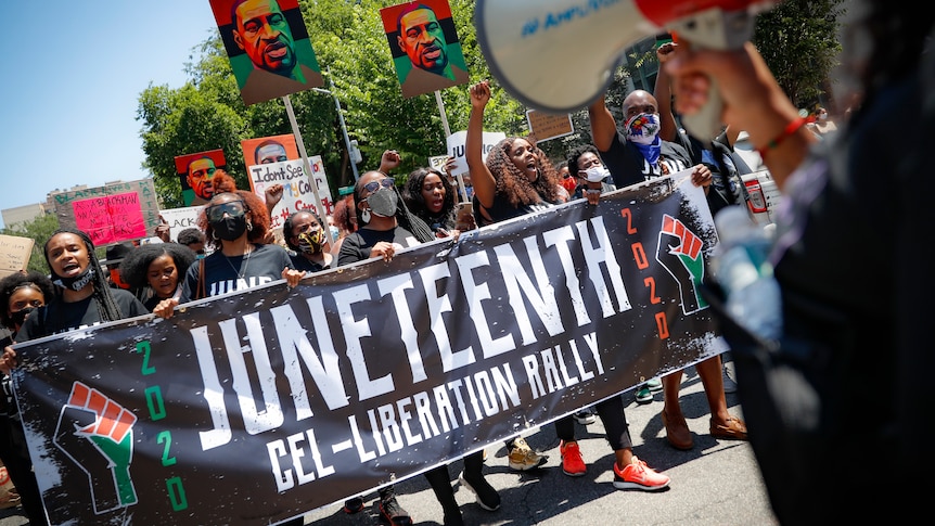 A crowd of people marching with a banner saying "Juneteenth".