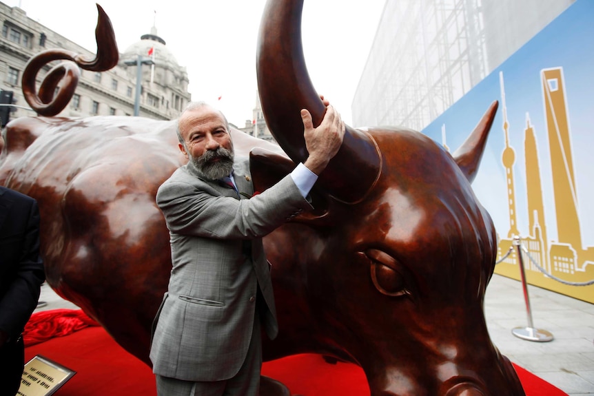 A man poses with the bronze Charging Bull statue