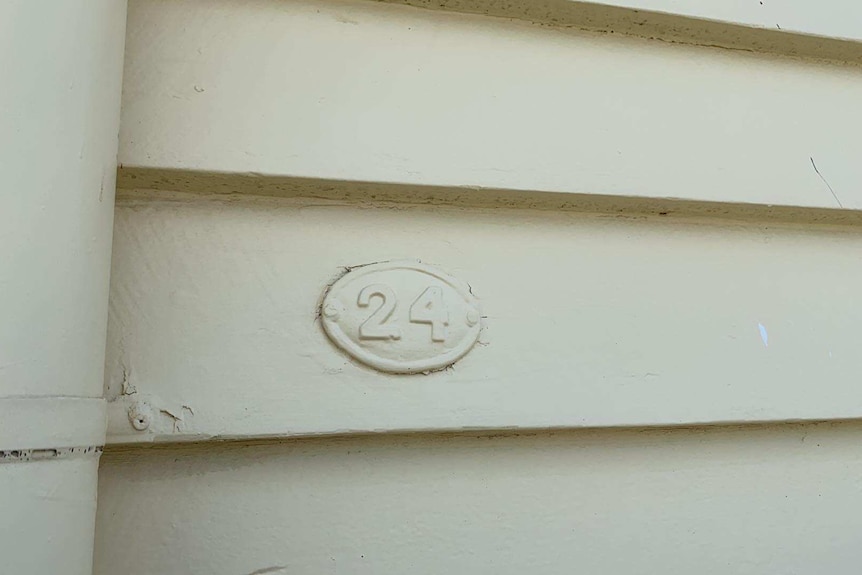 A house number painted in a cream colour, blends in with the weatherboards painted in the same colour.