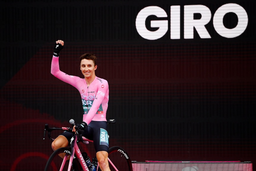 Jai Hindley holds his hand up and smiles in front of a black backdrop