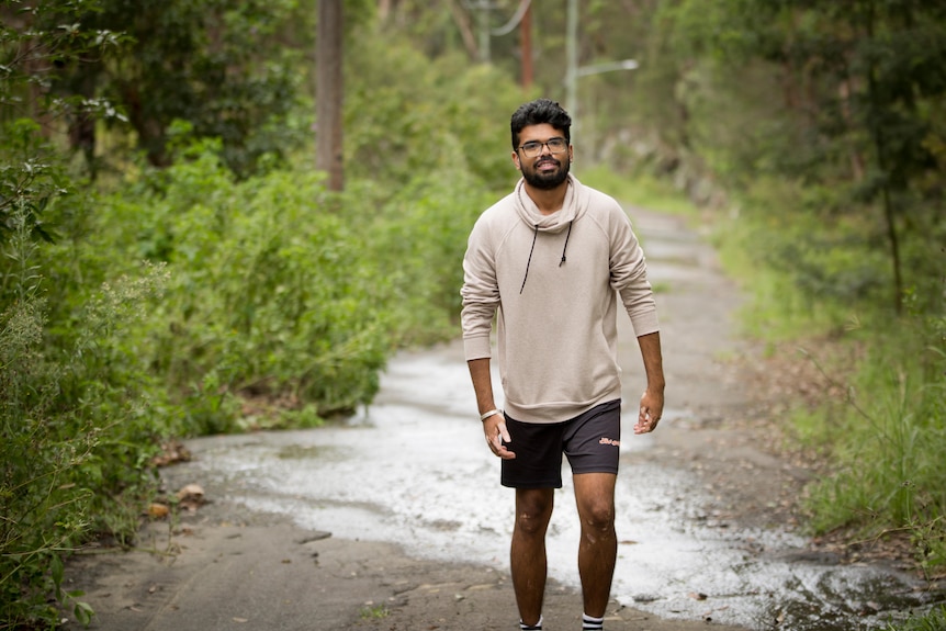 Arpit Charwal walks casually along a bush track surrounded by greenery. 