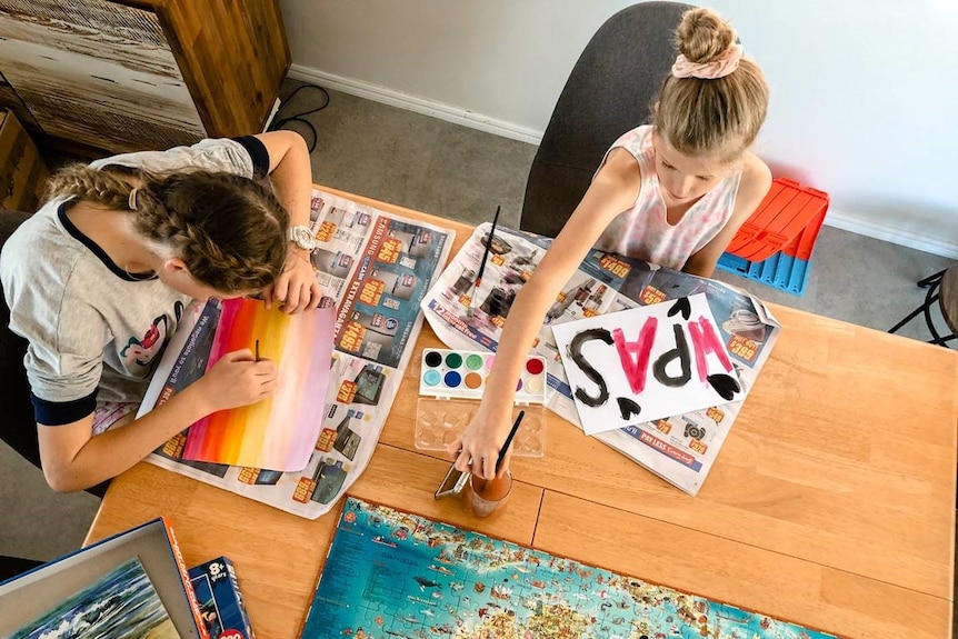 Birds-eye view of two girls paint at a dining room table