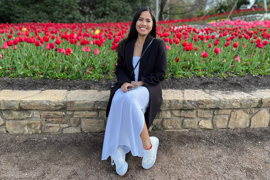 A woman sits near a garden.