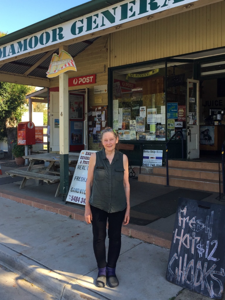 woman standing in front of a general store, smiling.