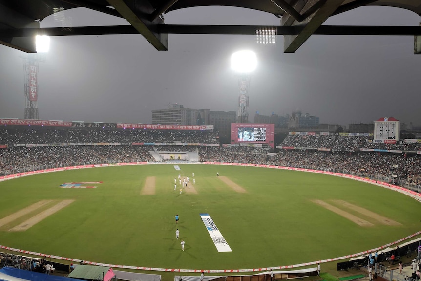 Floodlights on in a stadium and fans lighting their mobile phones during a day-night cricket Test.